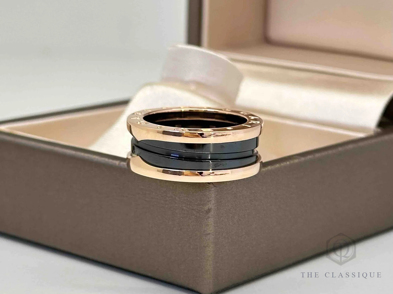 Nhẫn Bvlgari B.zero1 vàng hồng gốm đen đặt trên hộp, thấy rõ đường xoắn gốm và viền vàng
