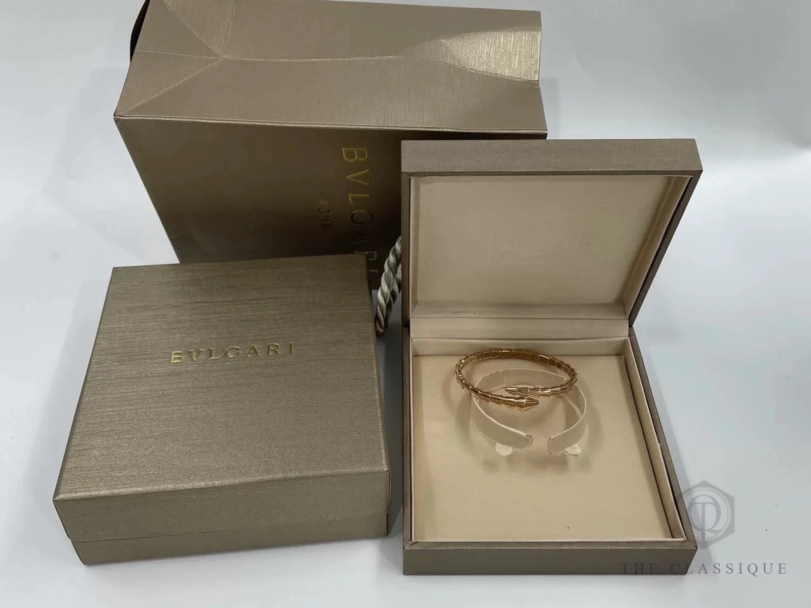 Vòng tay Bvlgari Serpenti Viper vàng hồng nằm trong hộp màu be, bên cạnh nắp hộp và túi giấy có chữ BVLGARI