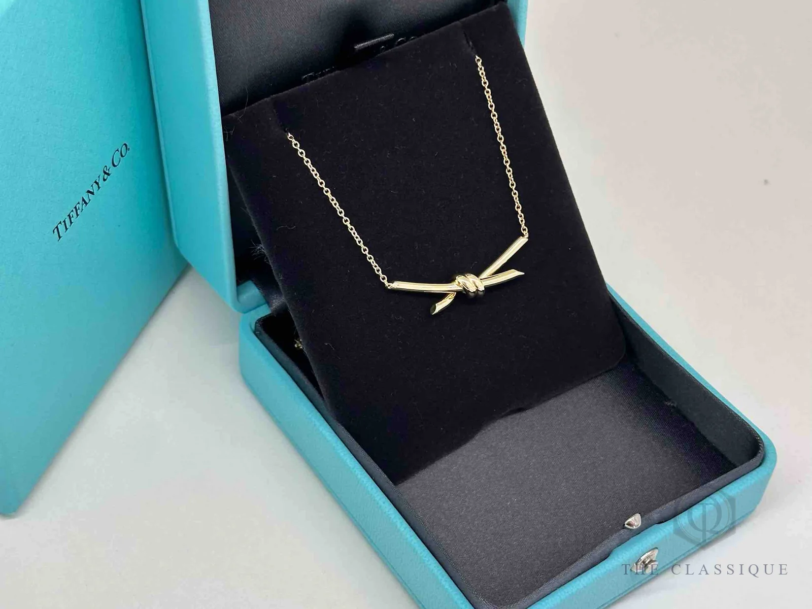 Hộp xanh Tiffany & Co. mở nắp, bên trong là dây chuyền Tiffany Knot vàng 18k