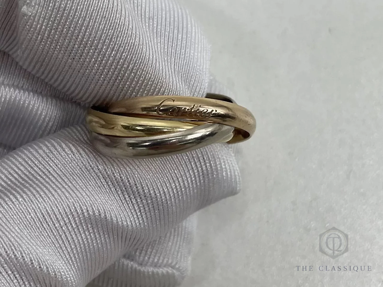 Nhẫn Cartier Trinity đeo trên tay có găng bông, nhìn nghiêng thấy chữ ký Cartier khắc trên một vòng