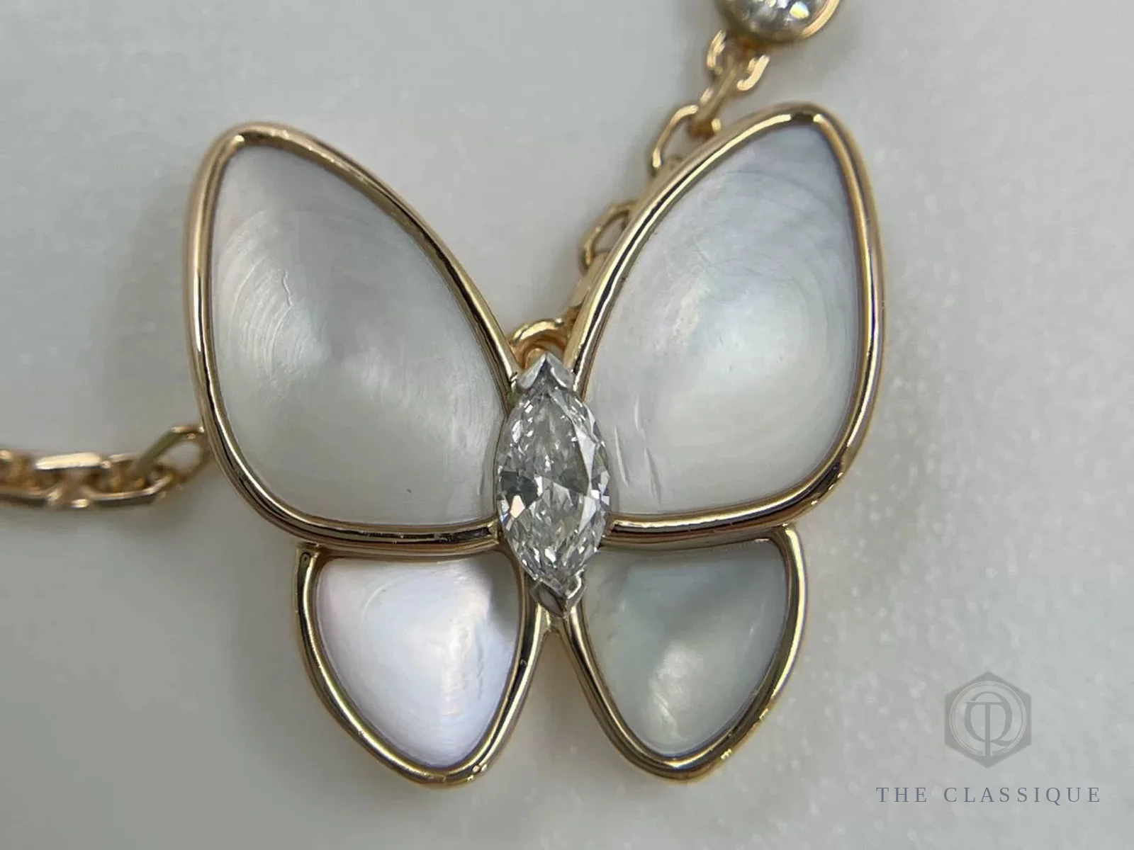 Cận cảnh mặt dây chuyền Van Cleef hình bướm bằng xà cừ, đính một viên kim cương và viền hạt vàng quanh cánh
