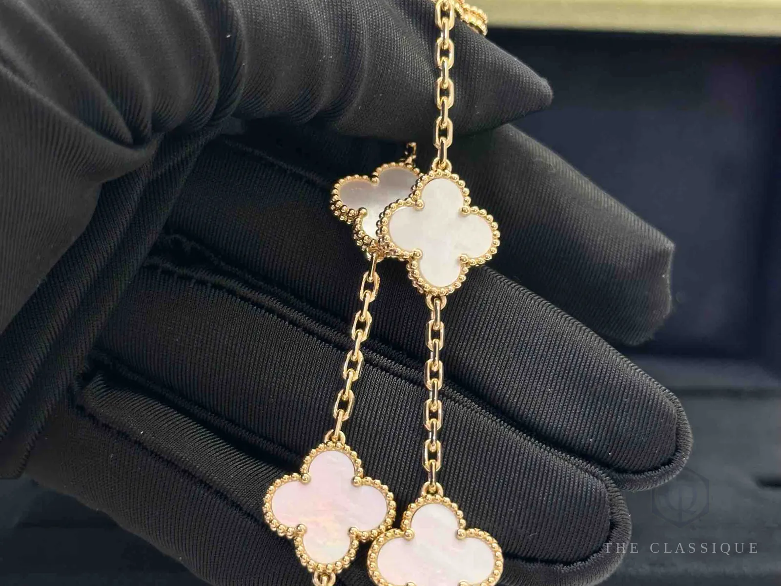 Người thẩm định đeo găng tay trắng cầm vòng tay Van Cleef Alhambra xà cừ để kiểm tra trước khi báo giá
