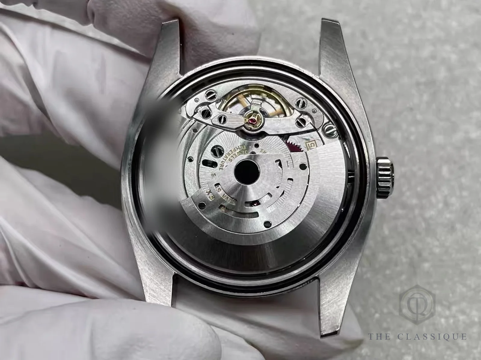 Người thẩm định đeo găng cầm vỏ đồng hồ Rolex đã mở nắp lưng, nhìn thấy bộ máy bên trong
