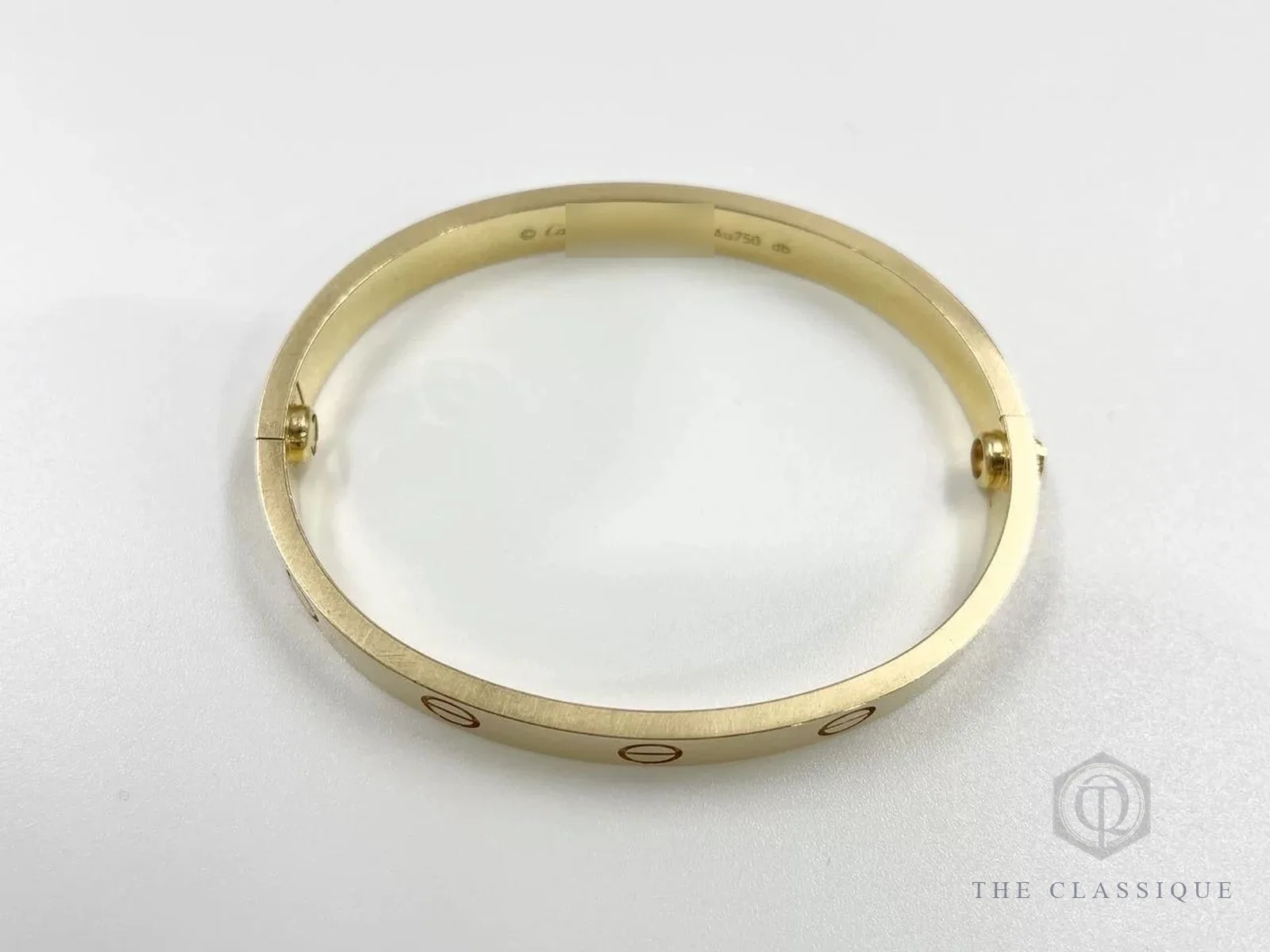 Vòng Cartier Love vàng vàng bản trơn đã qua sử dụng đặt trên nền trắng, thấy ốc vít ở hai bên thân vòng