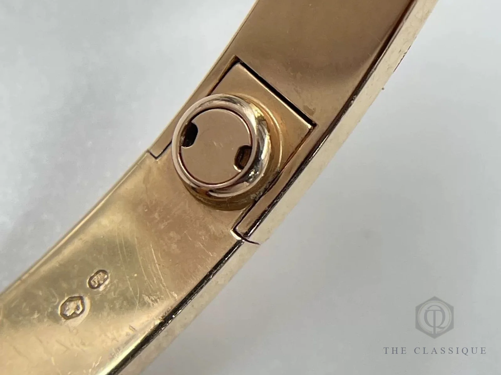 Cận cảnh ốc vít và bản lề mặt trong vòng Cartier Love vàng hồng cùng dấu kiểm định nhỏ trên thân