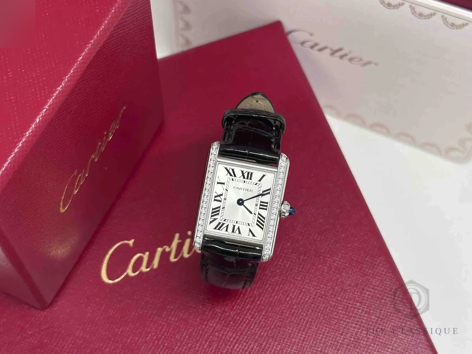 Đồng hồ Cartier thật giả, đồng hồ mặt vuông viền đính kim cương đặt trên hộp đỏ chính hãng tại The Classique