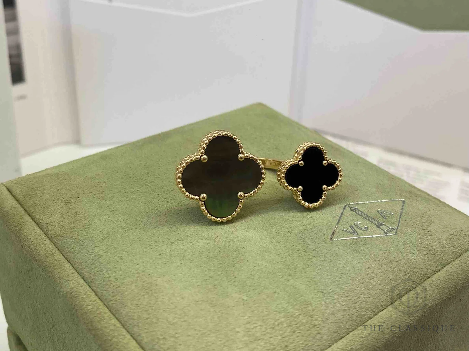 Nhẫn Van Cleef Alhambra hai motif mặt đá xám và đen, đặt cạnh dấu VCA đóng trên hộp