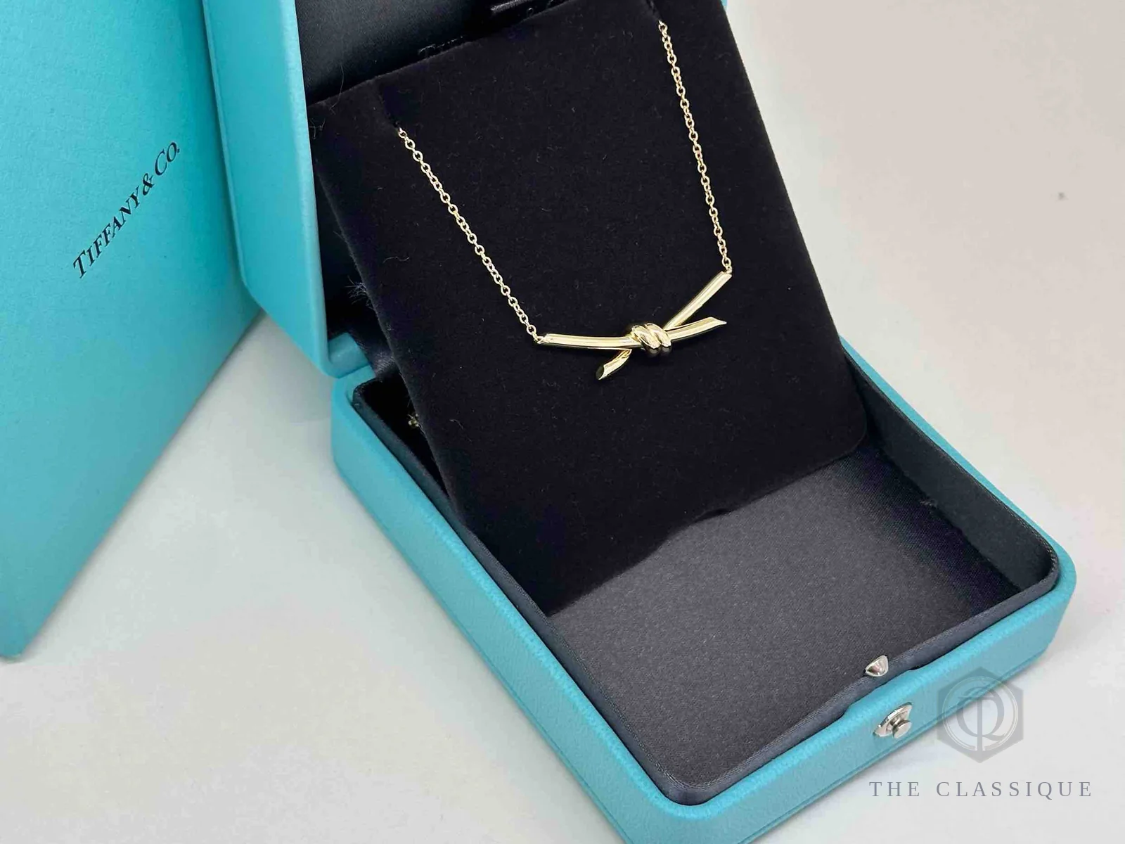 Dây chuyền Tiffany Knot vàng vàng trong hộp, thấy rõ độ dài dây và mặt nơ thắt nút