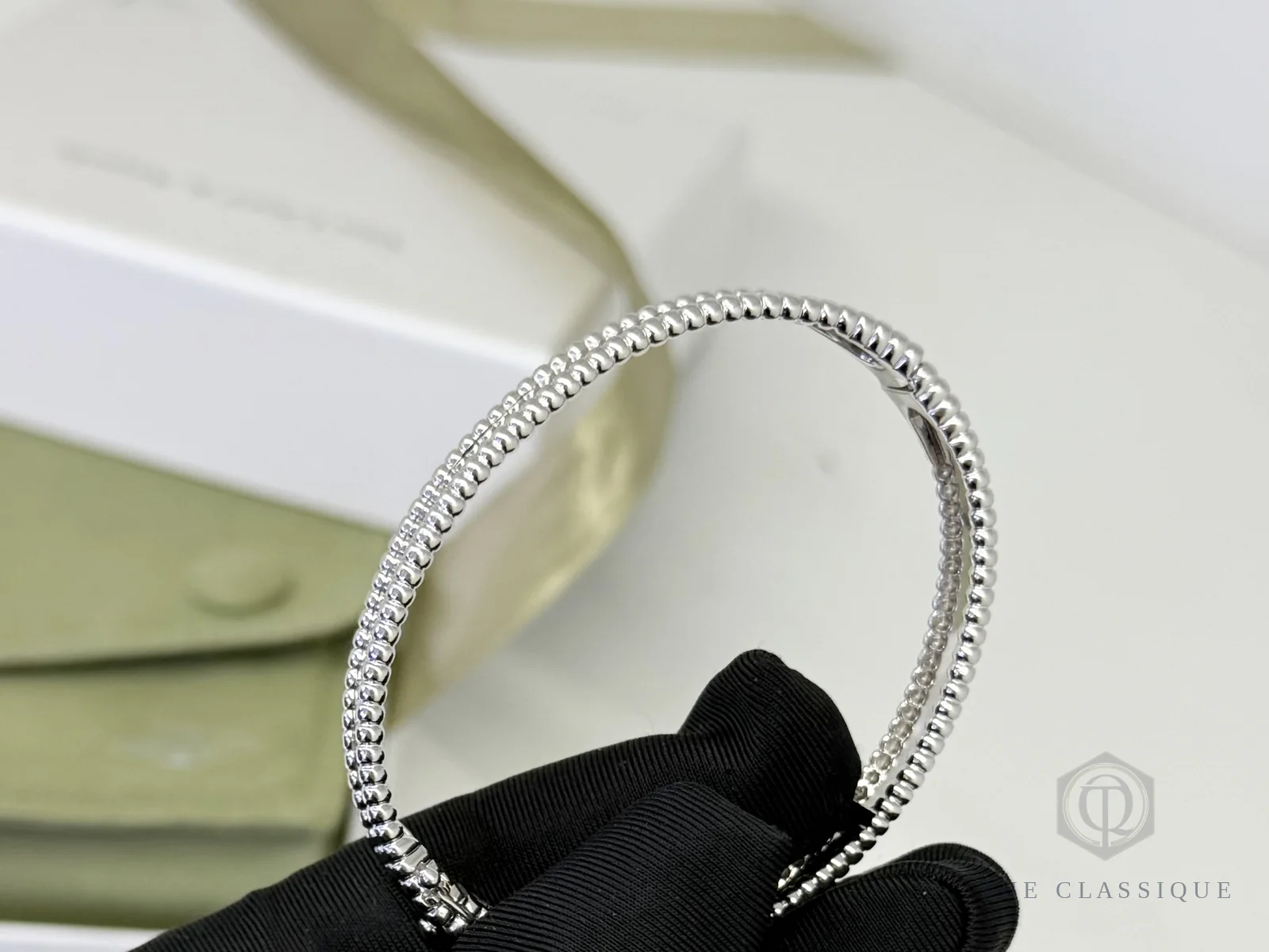 Vòng Van Cleef Perlée cầm trên tay, dây hạt vàng đều nhau và khoá bản lề mở hé