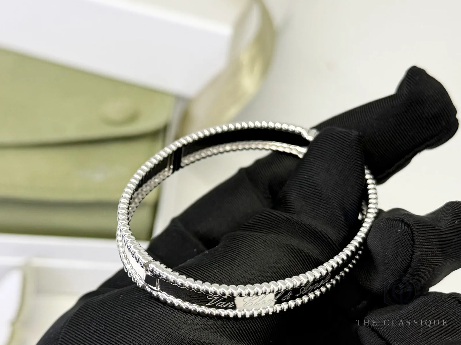 Vòng Van Cleef Perlée cầm nghiêng trên tay, thấy chữ khắc và khoá bản lề cạnh nhau